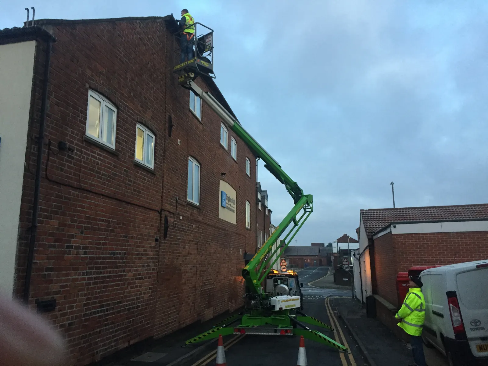 Cherry picker positioned beside a brick commercial building for high reach cleaning by Lanes Ltd